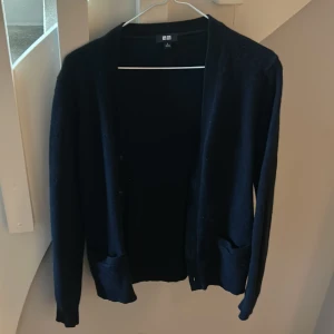 Mörkblå ullkofta från Uniqlo - Snygg mörkblå kofta från Uniqlo i 100% ull. Klassisk modell med långa ärmar, två fickor framtill och knäppning. Perfekt för lager-på-lager och passar till det mesta. Enkel och stilren design som funkar året runt.