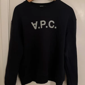 Marin crewneck från A.P.C.  - Marinblå crewneck från A.P.C. med klassisk rund hals och stor vit logotyp på bröstet. Tröjan är i mjuk bomull och har långa ärmar. Perfekt för en clean och stilren look. Inga som helst defekter bara blivit för liten!