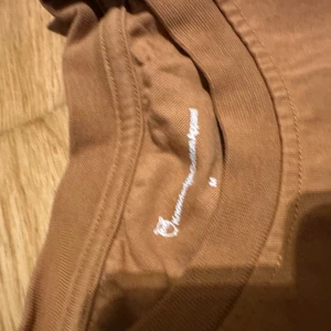 Brun t-shirt från Dedicated - Snygg brun t-shirt från Dedicated med rund hals och korta ärmar. T-shirten har en liten broderad logga på bröstet och är gjord i mjuk bomull. Perfekt basic-plagg med clean look och skön passform.