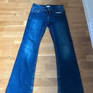 Blå bootcut jeans från Gina Tricot - Snygga blå jeans från Gina Tricot i klassisk bootcut-modell. Jeansen har normal midja, fem fickor och tydliga kontrastsömmar. Tillverkade i jeansmaterial med lätt slitning på låren för en cool look.