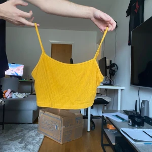 Gul ribbad croppad linnetopp - Snygg gul croppad linnetopp med tunna axelband och ribbad struktur. Perfekt för varma dagar och enkel att matcha med jeans eller kjol. Fräsch och trendig färg som verkligen poppar.