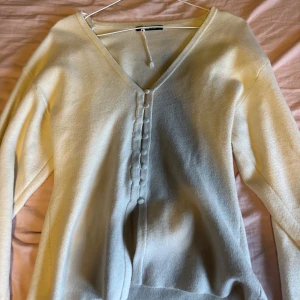 Kräm vit kofta med knappar från Gina Tricot - Kräm vit kofta från Gina Tricot med v-ringning och klädda knappar framtill. Långärmad och i mjukt material som känns skönt mot huden. Perfekt att slänga över en topp. Tröjan har dock en liten knappt synlig fläck som säkert enkelt går bort med fläckborttagning. Tröjan passar dig som har storleken S till L💞