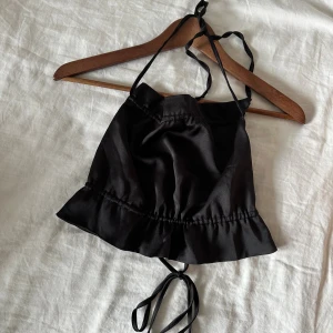 Svart satinlinnetopp från Gina Tricot - Supersnygg svart linnetopp i satin från Gina Tricot. Toppen har tunna axelband, volangkant nedtil. Öppen rygg🖤