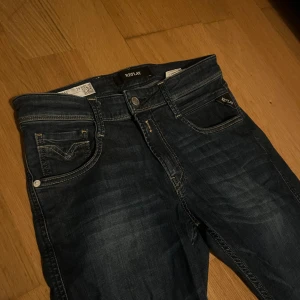 Replay Anbass jeans mörkblå stl 29 - Snygga mörkblå Replay Anbass jeans med klassisk femficksdesign och kontrastsömmar. Märkespatch bak i läderimitation och broderade bakfickor. Jeansen är i stretchigt denim och har en modern passform som sitter riktigt bra. Endast använda ett par gånger. Storlek 29/32