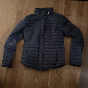 Svart dunjacka Michael Kors XS - Snygg svart dunjacka från Michael Kors i storlek XS. Jackan har quiltad design, hög krage och dragkedja framtill. Perfekt för kyliga dagar och har en stilren look med diskret logga på ärmen.