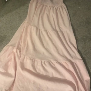 Ljusrosa långklänning med smock - Supersöt ljusrosa långklänning från 157 med smock upptill och volangiga lager. Klänningen är ärmlös och har en flowy passform som känns riktigt somrig. Perfekt för dig som gillar en romantisk och chill stil.