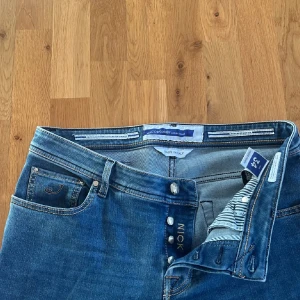 Jacob Cohen jeans, strl 34 - Snygga blå jeans från Jacob Cohen med klassisk femficksdesign och blå patch bak. Jeansen är slim fit i modellen nick.Perfekta för dig som gillar stilrena och tidlösa jeans. Mycket fint skick. Nypris 5500 SEK