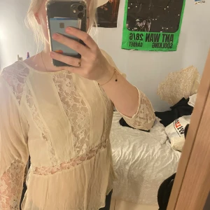 Beige spetsblus från H&M Divided - Säljer en romantisk beige blus från H&M Divided i storlek 40. Blusen har genomskinliga spetsdetaljer på ärmar, framstycke och midja, samt en liten knappöppning i nacken. Materialet är lätt och flowy, perfekt för dig som gillar en feminin vibe.