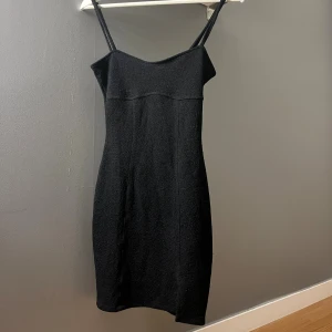 Svart kort klänning från H&M  - Svart figurnära klänning från H&M  i storlek XS. Klänningen har smala axelband, rak halsringning och en liten slits framtill. 