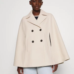 Beige cape-kappa från ONLY - Säljer denna helt nya  cape-kappa från ONLY prislapp sitter kvar nypris 629 kr!!! Kappan är beige med dubbelknäppning och klassisk krage. Jackan har en vid, svepande siluett och slitsar för armarna. Perfekt för dig som vill ha en stilren och trendig look med extra edge. Oversized i storleken