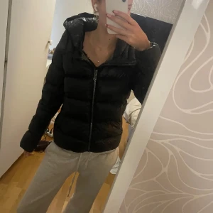 Svart pufferjacka från Colmar - Säljer en svart pufferjacka från Colmar med glansig finish och huva. Jackan har en tydlig dragkedja framtill och Colmar-logga på ärmen. Perfekt för kalla dagar och riktigt snygg till streetwear-stilen.