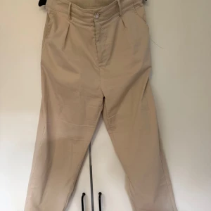 Beiga chinos -  beiga chinos med klassisk rak passform och pressveck framtill.  Köpta på secondhand hand, står varken storlek eller märke. Passar mig som är L, 176 cm lång.
