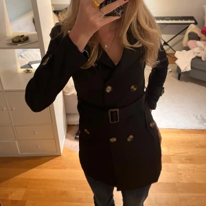 Svart trenchcoat med bälte och knappar - Snygg svart trenchcoat / kappa med fina knappar, bälte i midjan och i slätt o fint material. Går oxå att ha knäppt hela vägen som på bild 4! Perfekt nu till hösten 🩷skriv vid frågor