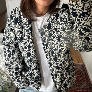 Jacka  - Säljer en quiltad bomberjacka med svartvitt blommigt mönster. Jackan har en loose passform, rund hals och dragkedja framtill. Materialet känns mjukt och jackan är perfekt för dig som gillar statement-plagg med cool vibe. Långärmad och riktigt skön att bära.