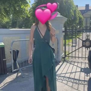 Grön balklänning med slits - Snygg jägargrön långklänning med omlottmodell och djup v-ringning. Klänningen har smala axelband som bildar ett X på ryggen och en elegant slits framtill som ger en flowy känsla. Perfekt för sommarens tillfällen när du vill sticka ut med en stilren look.