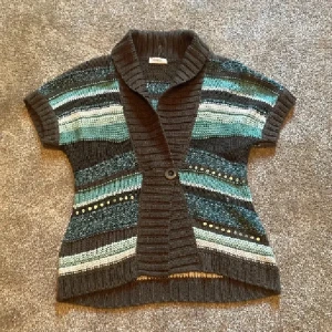 Randig stickad kofta från Bonita - Kortärmad stickad kofta från Bonita med bred krage och en knapp framtill. Randigt mönster i mörkbrunt, turkos, blått, vitt och beige. Snygga paljett-detaljer på framsidan. Perfekt att slänga över en t-shirt för en chill look. betalning med swish skickas spårbart 59kr