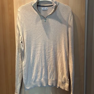 Beige half zip tröja Jack & Jones - Snygg beige långärmad tröja från Jack & Jones med half zip i halsen. Tröjan har ribbade muddar vid ärmslut och nederkant, och är gjord i mjuk bomull. Perfekt för dig som gillar stilren och enkel design.