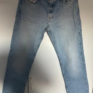 Ljusblå jeans från Jack & Jones 32/32 - Säljer ett par ljusblå jeans från Jack & Jones i klassisk rak modell. Jeansen har fem fickor, bruna kontrastsömmar och är tillverkade i bomull. Perfekta för dig som gillar en enkel och stilren look.
