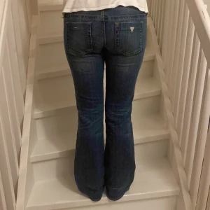 Blå bootcut jeans från Guess - Snygga blå jeans från Guess med klassisk bootcut-modell och låg midja. Jeansen har fem fickor, diskret slitning och logga på bakfickan. Riktigt jeans material och 2000s lågmidjade. Skriv om ni har frågor 🤗💕