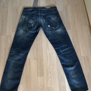 Blå dondup jeans med lite stilrena slitningar. - Snygga blå jeans från Dondup i modell med slitningar och tvättade detaljer. Klassisk femficksdesign, kontrastsömmar och raka ben. Jeansen har en cool, lite sliten look och är perfekta för dig som gillar streetstyle. Materialet är robust denim.