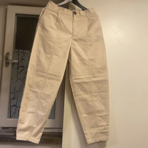 Beiga chinos från Zara med raka ben - Snygga beiga chinos från Zara med vida ben och hög midja. Byxorna har pressveck framtill, två bakfickor och stängs med knapp och dragkedja. Tillverkade i mjuk bomull för en bekväm känsla och stilren look. Har använts endast 2 gånger.