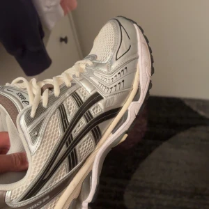 Asics Gel-Kayano vita och silver sneakers - Säljer ett par Asics Gel-Kayano sneakers i vitt och silver med svarta detaljer. Skorna har mesh-överdel för bra andningsförmåga, klassisk snörning och en chunky sula med dämpning. Perfekta för dig som gillar sportig och trendig stil. Anledningen till att detta säljs är då jag fick exakt samma par av min pappa i födelsedagspresent dessa är använda ett fåtal gånger. Nypris på dessa ligger på 1900 och jag kan tänka mig att gå ned från 1000 vid en snabb affär. Vid behov skriv pm för bättre bilder.