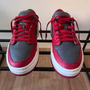 Nike Air Jordan 1 Low röd/grå - Säljer ett par Nike Air Jordan 1 Low sneakers i rött och mörkgrått skinn med vit och röd sula. Klassisk siluett med snörning, rund tå och lågt skaft. Swoosh-logga på sidan och broderad Air Jordan-logga på hälen. Perfekta för dig som gillar streetstyle. Utan box, använd få gånger