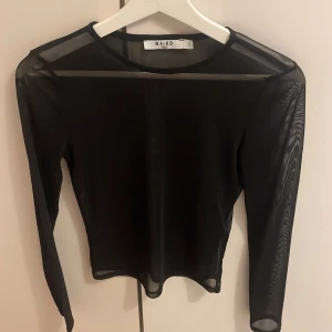 Svart mesh topp från NA-KD - Säljer en svart mesh topp från NA-KD med lång ärm och rund halsringning. Tunn och genomskinlig, perfekt att styla lager på lager. Snygg och enkel design som passar till många olika looks.
