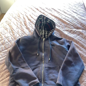 Marinblå hoodie med dragkedja från Burberry - Snygg marinblå hoodie från Burberry använd och färgen är inte som den är på bilderna den börjar försvinna lite men inget som man lägger märke till. En dragkedja bit har försvunnit men den funkar fortfarande att dra up och ner. 
