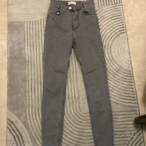 Grå skinny jeans från Zara, strl 34 - Snygga grå jeans från Zara i storlek 34. Modellen är skinny med hög midja och klassiska fem fickor. Jeansen har dragkedja och knapp framtill samt bälteshällor. Perfekta för en trendig och stilren look.