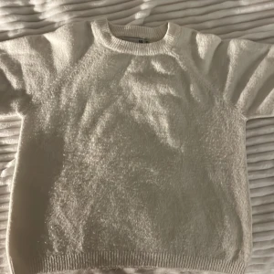 Vit  stickad tröja 157 - Mysig vit stickad tröja från 157 med fluffig känsla och rund hals. Tröjan har ribbade muddar vid hals, ärmslut och nederkant. Perfekt för lager-på-lager under kyliga dagar.