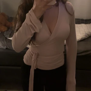 Beige omlottopp från Gina Tricot - Supersnygg beige omlottopp från Gina Tricot med långa ärmar och knyt i midjan. Toppen har v-ringning och sitter figurnära, perfekt för dig som gillar en stilren och trendig look.