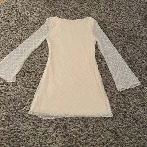 Kort spetsklänning med vida ärmar - Superfin ljus kort klänning med transparenta, vida långärmar och prickigt spetsmönster. Klänningen har en rak passform men lite utsvängd nedtill.