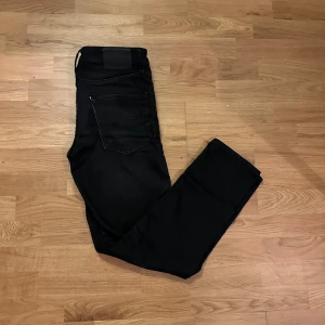 Svarta jeans från Jack & Jones - Svarta jeans från Jack & Jones, modell Comfort/Mike. Klassisk femficksdesign med svarta sömmar och diskret logopatch bak. Jeansen har rak passform och är tillverkade i mjukt bomullsmaterial med lite stretch för extra komfort.