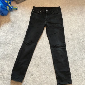 Svarta Levi's 511 jeans W30 L32 - Svarta jeans från Levi's modell 511 med klassisk femficksdesign och smal passform. Jeansen har en snygg mörk ton, diskreta nitar och dragkedja i gylfen. Perfekt för dig som gillar stilrena och tidlösa jeans med modern siluett.