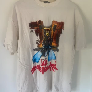 Kanye west t-shirt  - Vit t-shirt med tryck från Kanye Wests 'Late Registration' och 'Touch the Sky Tour 2005'. Framsidan har ikonisk björn-grafik och röd text, baksidan listar turnéstäder. Klassisk passform och rund hals. Perfekt för fans av hiphop och streetwear.