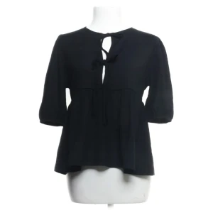 Svart blus med knyt från 157 - Svart blus från 157 med trekvartsärmar och snygg knytning framtill vid halsen. Modellen är lite lösare och har en lätt rynkad midja som ger en avslappnad siluett. Perfekt för dig som gillar stilrena och enkla plagg med en twist.