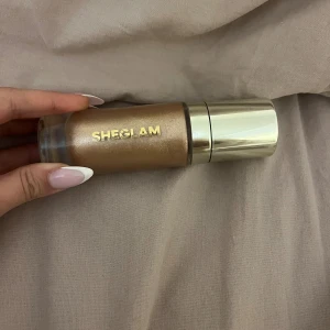 Sheglam flytande highlighter guld - Flytande highlighter från Sheglam i en snygg guldig nyans. Kommer i en genomskinlig flaska med silvrig pump och lock. Perfekt för att ge huden en glowig och skimrande finish. Använt 2 gånger 
