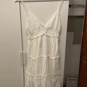 Vit sommarklänning från Bershka - Superfin vit kortklänning från Bershka med tunna axelband och v-ringning. Klänningen har volangdetaljer och är sydd i ett lätt, krinklat bomullstyg som ger en avslappnad vibe. Perfekt för varma dagar och enkel att styla med sandaler eller sneakers. Aldrig använt, säljer för att den var för liten🤗🤗