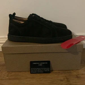 Svarta sneakers från Christian Louboutin - Snygga svarta sneakers från Christian Louboutin med klassisk röd sula och diskret logga undertill. Skorna har rund tå, snörning och är tillverkade i mjuk mocka som ger en lyxig känsla. Perfekta för dig som vill ha en stilren och exklusiv look.