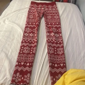 Röda leggings med vintermönster - Mysiga röda leggings med vita snöflingor, hjärtan och zigzag-mönster. Perfekta för vintersäsongen och jul, med hög midja och stretchigt material som sitter skönt. Passar dig som vill ha något både snyggt och bekvämt under kalla dagar.