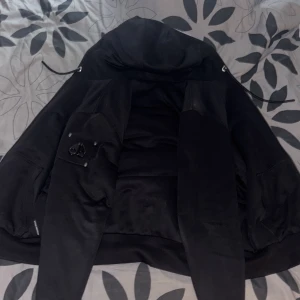 Svart pufferjacka från Moose Knuckles - Säljer en svart ClassicBunny från Moose Knuckles med ikonisk logga på ärmen och quiltat innerfoder. Jackan har huva med dragsko och snygga detaljer i metall. Koftan har ett litet hål inuti under högra armhålan men det går o fixa jätte enkelt om man kan sy eller skicka den till någon skräddare annars är det inget problem. Koftan har en clean look. Har haft koftan cirka 1 år. Är mer än nöjd o sälja den för 1500😁