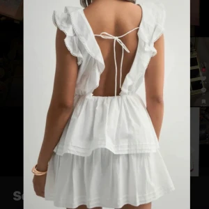 Vit volangklänning med öppen rygg - Supersöt vit kortklänning med volanger, omlott framtill och öppen rygg med knytband. Aldrig använd!