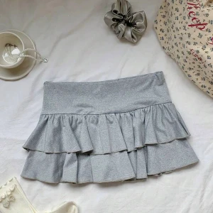 Grå volangkjol  - Supersöt grå kjol med dubbla volanger och bred midja. Kjolen sitter lågmidjat och har inbyggda shorts💗