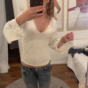 Vit blus med broderade vida ärmar - Säljer en vit blus med djup v-ringning och vida, broderade ärmar. Toppen är insydd så är egentligen lite bredare o de kan man ta bort ifall man vill, har snygga detaljer med svart broderi på ärmarna. Knappt använd.