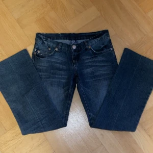 Lågmidjade Victoria Beckham jeans - Snygga blå jeans från Victoria Beckham i storlek 27. Modellen har raka/utsvängda ben och låg midja, med coola silverfärgade kronbroderier på bakfickorna och slitningar framtill. Klassisk femficksdesign och detaljerade nitar. Perfekt för dig som gillar statement-plagg. Dom är i väldigt bra skick och snygga som fan💕. Lite små slitningar vid kanterna av framfickorna men det är inget som märks av. Säljer då dom tyvär är för små för mig😭😭