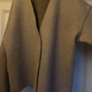 Kappa från Vila - Säljer en stilren beige kofta från Vila i storlek 34. Koftan har en öppen design utan synliga knappar, lång ärm och är gjord i ett mjukt material som känns skönt mot huden. Perfekt för lager-på-lager och enkel att matcha med olika outfits.