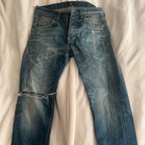 Blå Lee jeans  - Säljer ett par blå jeans från Lee i modellen Straight Jeansen har klassisk femficksdesign, slitningar och hål på benet och bakfickan för en cool, avslappnad look. Tillverkade i 100% bomull med rak passform och normal midja.
