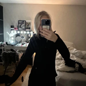 Svart vindjacka med huva från H&M Sport - Svart vindjacka från H&M Sport i storlek XS. Jackan har huva, dragkedja framtill och är långärmad. Snygg och enkel design med smal passform, perfekt för blåsiga dagar. Materialet är lätt och känns sportigt.