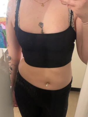 Svart croppad linnetopp - Svart croppad linnetopp med ribbad struktur. Toppen har korsade band i ryggen och sitter tight mot kroppen. 